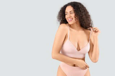 Gri arka planda zarif pembe iç çamaşırlı güzel, mutlu, Afro-Amerikan kadın.