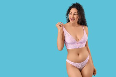 Mavi arka planda zarif pembe iç çamaşırlı güzel, mutlu, Afro-Amerikan kadın.