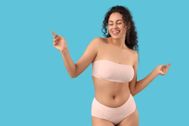 Mavi arka planda zarif pembe iç çamaşırlı güzel, mutlu, Afro-Amerikan kadın.