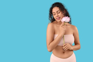 Güzel, mutlu, Afro-Amerikalı, zarif pembe iç çamaşırlı, mavi arka planda şakayık çiçekli bir kadın.