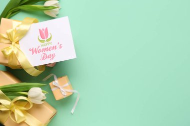 Turkuaz arka planda hediye kutuları ve lalelerle dolu bir kartpostal. Mutlu Kadınlar Günü