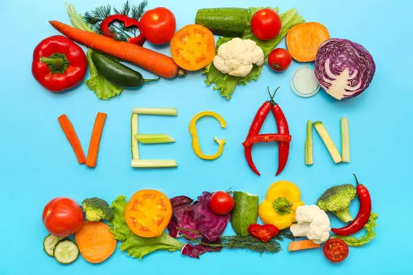 Renk arkaplanında VEGAN ve farklı sebzeler içeren kompozisyon