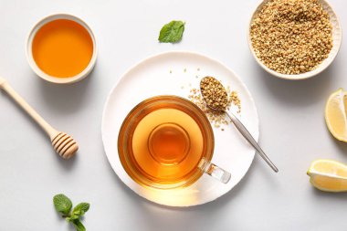 Bir bardak sıcak karabuğday çayı, limon, nane ve bal, gri arka planda.