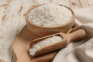 Beyaz ahşap arka planda çiğ pirinçli kase ve kepçe.