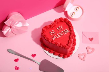 Hediye kutusu, zarf ve pembe arka planda nişan yüzükleri olan tatlı bento pastası. Sevgililer Günü kutlaması