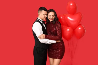 Kırmızı arka planda kalp şeklinde balonları olan, sevgi dolu genç bir çift. Sevgililer Günü 'nün kutlaması