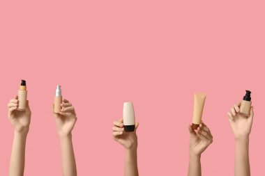 Şişeli kadın elleri ve pembe arka planda makyaj malzemeleri.