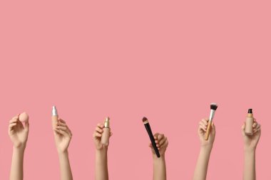 Makyaj malzemesi şişeleri, fırçalar ve pembe arka planda sünger olan kadın elleri.