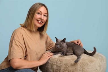 Orta yaşlı bir kadın, sevimli bir kedinin yanında oturuyor mavi arka planda.