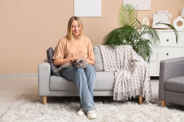 Evdeki kanepede oturan kedisi olan orta yaşlı bir kadın.