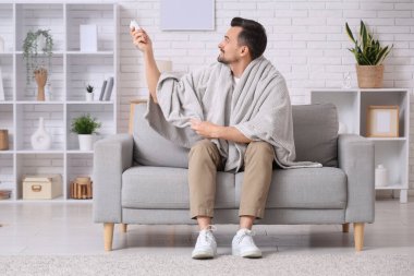 Oturma odasındaki kanepede oturan klimalı uzaktan kumandalı yakışıklı genç adam.