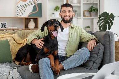 Dobermann 'ın köpeği evdeki kanepede oturan genç adam.