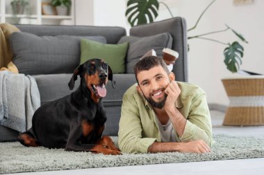 Dobermann 'ın köpeği evde halıya uzanmış genç bir adam.