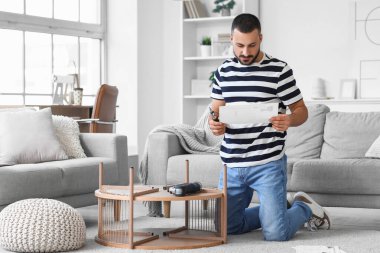 Evde kahve masasını elle monte eden genç bir adam.