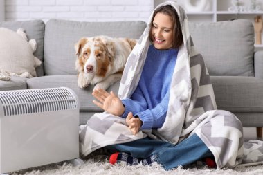 Battaniyeli genç bir kadın ve ısıtıcının yanında oturan Avustralyalı çoban köpeği.