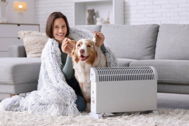 Battaniyeli genç bir kadın ve ısıtıcının yanında oturan Avustralyalı çoban köpeği.