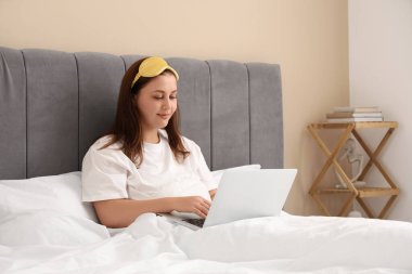 Sabahları dizüstü bilgisayarı olan güzel genç bir kadın yatakta yatıyor.