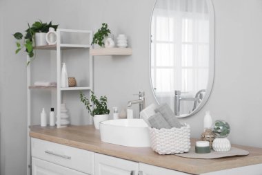 Katlanmış temiz havlular, ev bitkileri ve kozmetik ürünleri banyodaki masada duran hasır sepet.