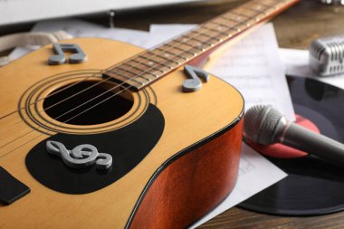 Tahta masa üzerinde nota işaretleri, mikrofon ve nota kağıtları olan bir gitar.