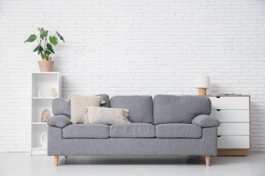 Beyaz tuğla duvarın yanında rahat kanepesi, şifoniyeri ve raf ünitesi olan şık bir oturma odası.