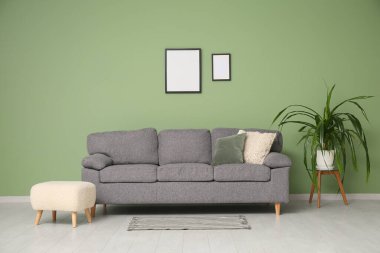 Yeşil duvarın yanında rahat kanepe, puf ve çiçekli şık bir oturma odası.