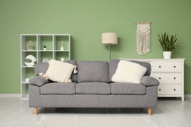 Yeşil duvarın yanında rahat kanepesi, raf ünitesi ve şifoniyeri olan şık bir oturma odası.