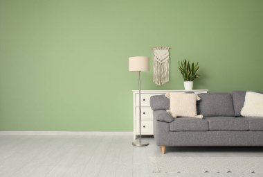 Yeşil duvarın yanında rahat kanepesi, lambası ve şifoniyeri olan şık bir oturma odası.