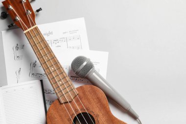 Ukulele, mikrofon, nota kağıtları ve gri arkaplan üzerine not defteri