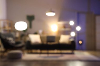 Karanlık oturma odası, siyah kanepe, koltuk ve geceleri parlayan lambalar.