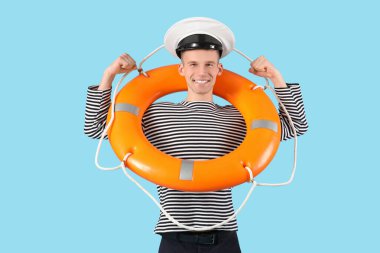 Kurtarma yüzüklü erkek denizci mavi arka planda kaslarını gösteriyor.