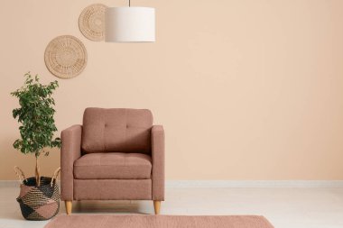 Oturma odasında bej duvarın yanında ağaç ve tavan lambası olan rahat bir koltuk. Tasarım için pankart