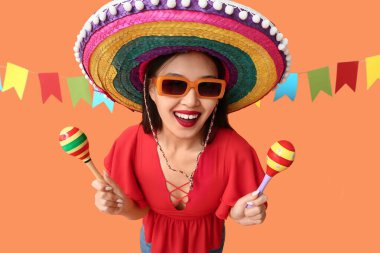 Meksika şapkalı ve turuncu arka planda marakas giyen mutlu genç kadın.