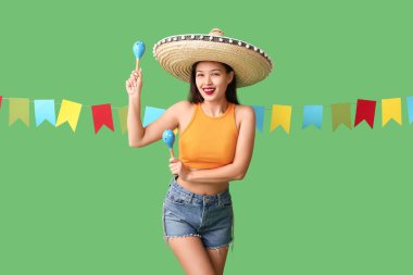 Meksika şapkalı mutlu genç kadın, marakas ve yeşil arka planda çelenk