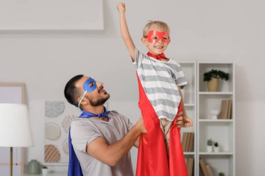Mutlu bir baba ve süper kahraman gibi giyinmiş küçük oğlu evde eğleniyor.