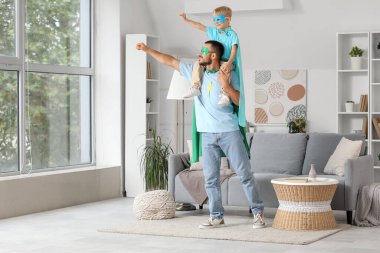 Mutlu bir baba ve süper kahraman gibi giyinmiş küçük oğlu evde eğleniyor.