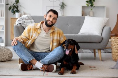 Genç adam evde Dobermann 'ın köpeğine sarılıyor.
