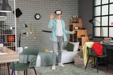 Erkek öğrenci yatak odasında VR gözlüğü kullanıyor.