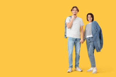 Kot ceketli genç çift sarı arka planda el ele tutuşuyorlar.