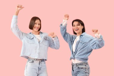 Kot elbiseli genç kadınlar pembe arka planda dans ediyorlar.