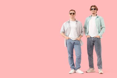 Pembe arka planda güneş gözlüklü kot giyen genç adamlar.