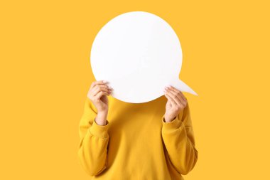 Sarı arka planda boş konuşma balonu olan genç bir kadın.