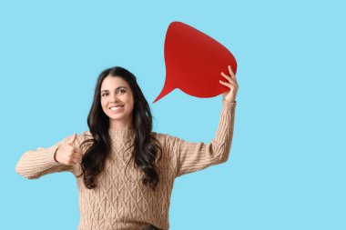 Boş konuşma baloncuğu olan genç bir kadın mavi arka planda baş parmağını kaldırıyor.