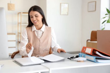 Ofiste belgelerle çalışan genç bir iş kadını.