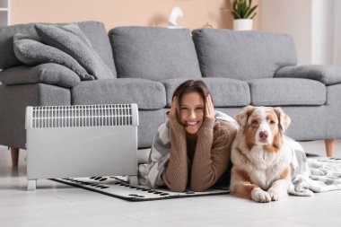 Battaniyeli genç kadın ve Avustralyalı çoban köpeği ısıtıcının yanında yerde yatıyor.