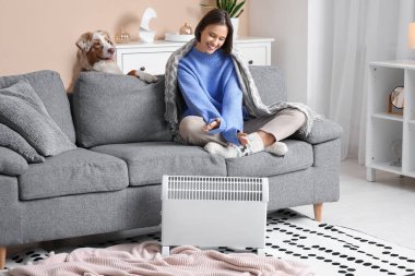 Battaniyeli genç kadın ve kaloriferin yanında ısıtan Avustralyalı çoban köpeği.