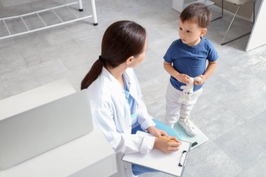 Klinikte tartıya ağırlığını koyan küçük tatlı bir oğlu olan kadın bir çocuk doktoru.