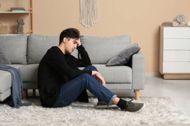 Evdeki halıda oturan depresif genç adam.