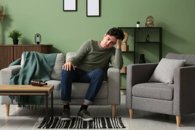 Evdeki kanepede oturan bunalımlı genç adam.