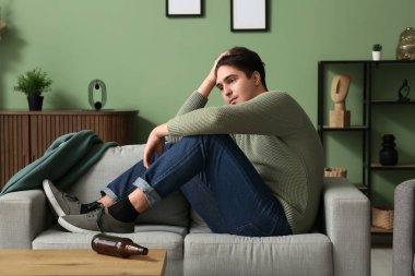 Evdeki kanepede oturan bunalımlı genç adam.