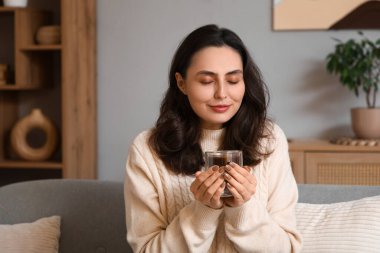 Evdeki kanepede oturan bir fincan sıcak çikolatalı güzel, genç ve mutlu kadın.